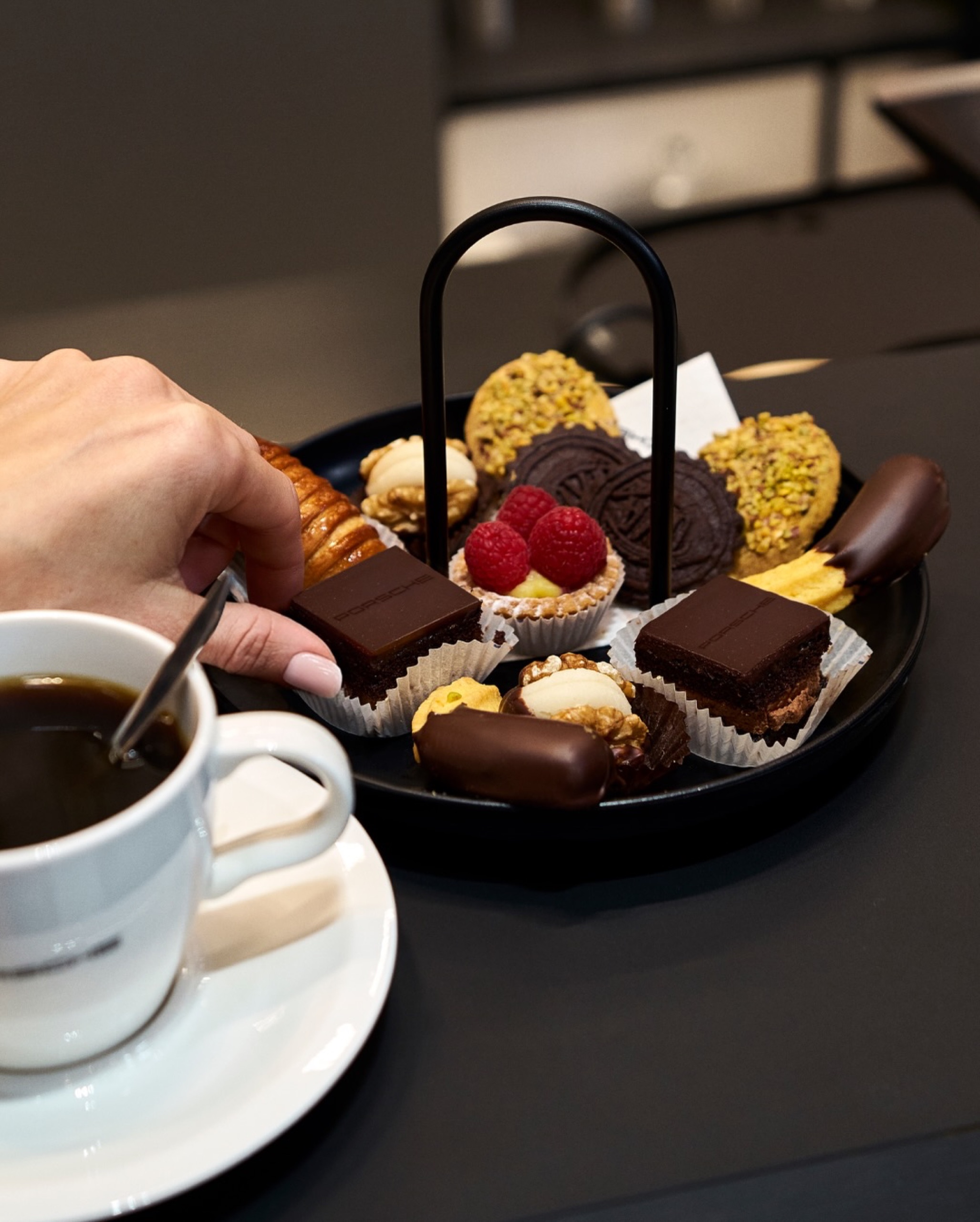 Hand holding a coffee cup at the Porsche Café counter, 2